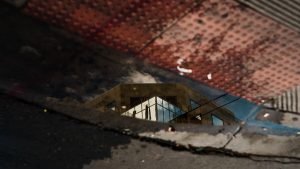 Reflection of a modern architectural building in a sidewalk puddle with textured surfaces.